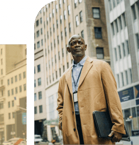  African man in professional clothing stands outdoors against a New York City skyline, appearing thoughtful and composed