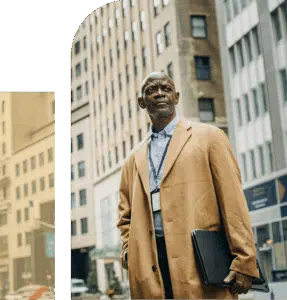  African man in professional clothing stands outdoors against a New York City skyline, appearing thoughtful and composed