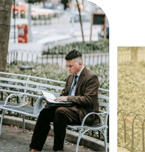  An Asian man sits on a bench reviewing a book and a calendar, focused and overwhelmed, with trees and open space behind him