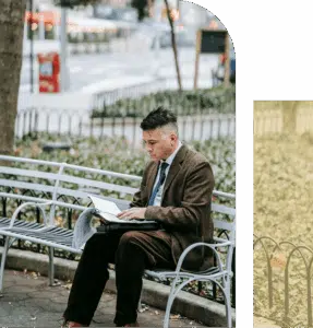 An Asian man sits on a bench reviewing a book and a calendar, focused and overwhelmed, with trees and open space behind him