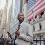 High-functioning South African man smiles while holding a phone outside New York City after burnout therapy in New York City