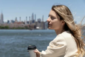 A woman works in a minimalist office or café, holding documents and a phone while concentrating on multiple responsibilities