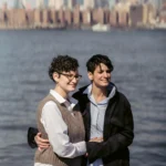 A woman rests her head on a desk beside an open laptop and glasses, eyes closed, showing mental fatigue after long work hours