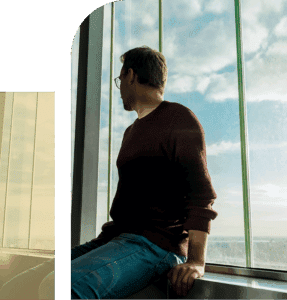 Man seated beside a window with his back to the camera, natural light outlining a quiet, introspective moment