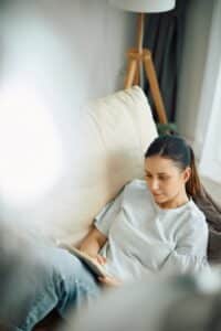 Woman sitting on a sofa reading a book, relaxed posture and quiet space suggesting rest and mental ease