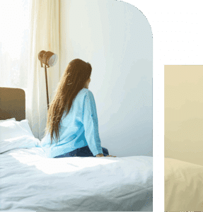 Woman sitting up on a bed after waking, viewed from behind, capturing early morning stillness and transition