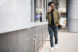 An African American man walking outside a building while talking on the phone, smiling in a casual moment