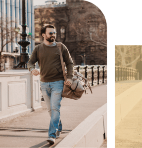 Man holding a duffel bag, looking to the side with a relaxed smile in an urban outdoor setting