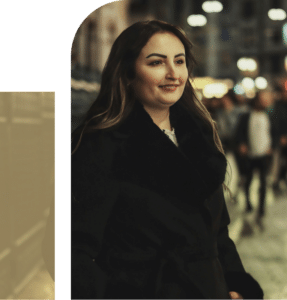 Woman in a black coat walking at night, soft lighting and a slight smile creating a quiet, reflective mood