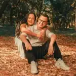 A woman works in a minimalist office or café, holding documents and a phone while concentrating on multiple responsibilities