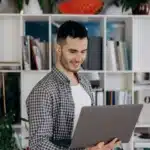 A professional man smiling while working on a laptop at a desk in a modern office space, focused yet relaxed during his workday