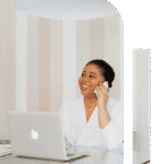 African American professional woman smiling with laptop open and phone to her ear during a focused work call today here!
