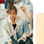 Woman painting with hair tied up, smiling as she looks down at her artwork, enjoying a quiet, creative moment of focus