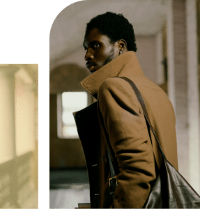 African American man holding a bag, standing inside a modern building hallway, looking thoughtful in soft indoor light
