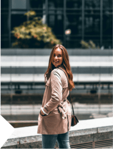 A woman smiling and looking back near city buildings, expressing confidence, progress, and personal growth.