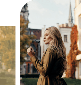 Blonde woman wearing sunglasses outdoors with a gentle smile, standing in daylight with a relaxed, confident presence