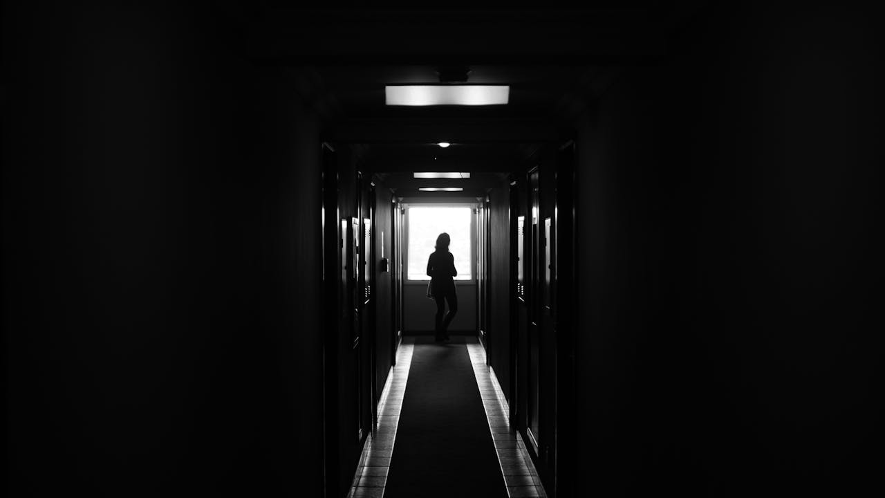 Silhouette standing alone in a dark hallway representing isolation caused by imposter syndrome and perfectionism