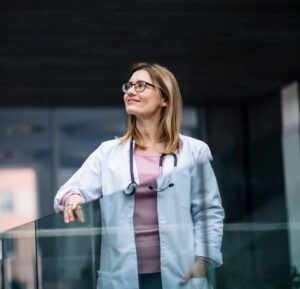 Female doctor in lab coat smiling confidently while looking aside, representing calm, professionalism, and care