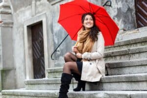 Woman with red umbrella sitting on city steps smiling softly and looking aside in bright daylight in New York City view