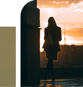 A woman standing on a rooftop at sunset, overlooking the city skyline, with warm light creating a quiet reflective moment
