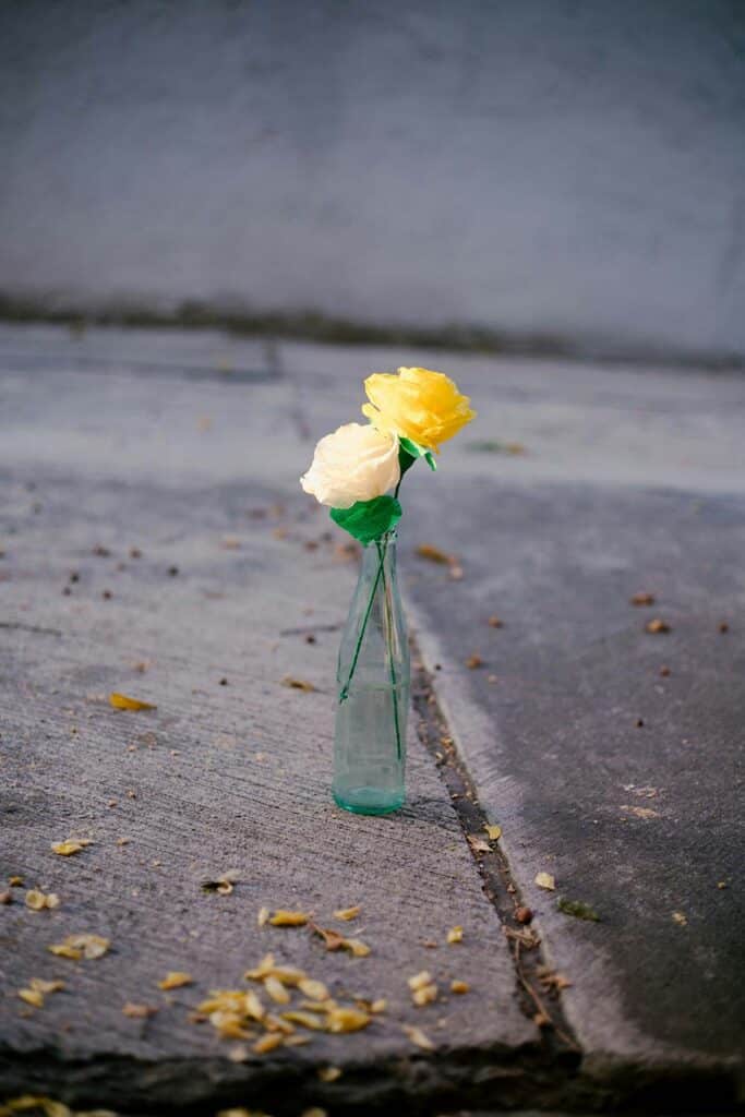 A slender glass bottle sits on a weathered concrete surface, holding two artificial roses
